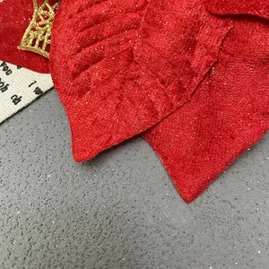 Gros plan détaillé d'une fleur de Noël en velours diamant rouge et paillettes dorées.