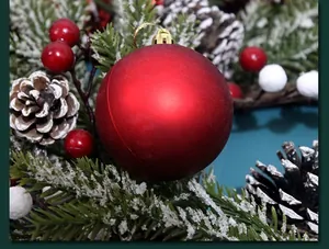 Close-up of red matte Christmas ornament ball with gold hanging loop in festive wreath