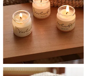 Close-up of three lit travel size scented candles in clear glass jars with labels