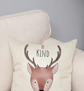 Dettaglio della fodera per cuscino con cervo e scritta 'Be Kind' su un divano color crema