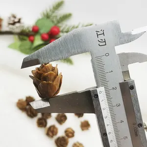 Detailed view of a small brown artificial pine cone accessory showing size with a caliper