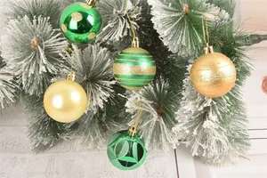 Primo piano di varie palline di Natale verdi e dorate su un pino innevato decorato.