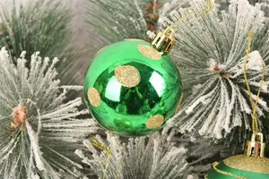 Primo piano di palla di Natale verde con pois glitterati dorati su rami di pino innevati.