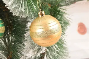 Primo piano di una palla di Natale dorata a strisce glitter appesa a un ramo innevato.