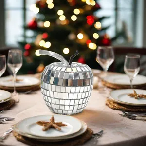 Verspiegelter silberner Apfel-Diskokugel-Deko auf festlichem Tisch mit Weihnachtsbaum-Hintergrund