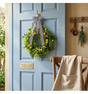Ghirlanda verde artificiale con limoni e nastro a righe su una porta di legno blu