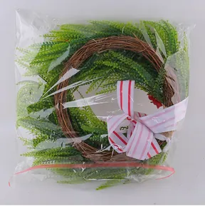 Artificial green foliage wreath with striped ribbon bow in transparent packaging.