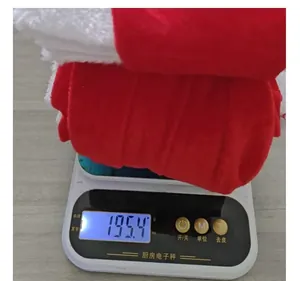 Gros plan détaillé d'un costume de Noël en velours rouge pesant 195,4 g sur une balance de cuisine