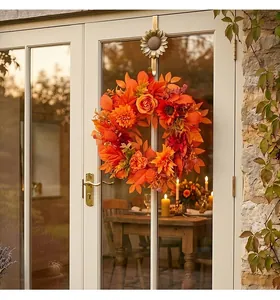 Ghirlanda autunnale con foglie d'acero arancioni e fiori appesa a una porta a vetri.