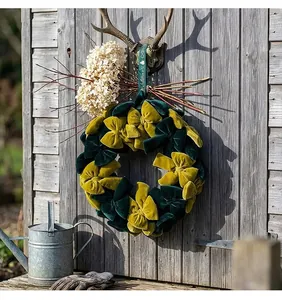 Detalle de una corona navideña de terciopelo con lazos verdes y amarillos en una puerta rústica.