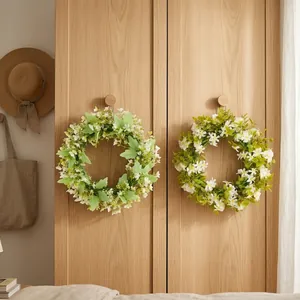 Two lush green artificial wreaths with white flowers hanging on a wooden cabinet door.