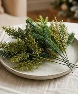 Realistic artificial pine and fern branches displayed on a ceramic plate for holiday decor.
