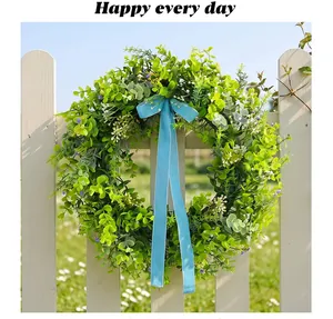 Close-up of artificial green leaf wreath with blue velvet ribbon on white fence