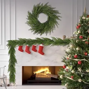Artificial green pine needle wreath and garland set decorating a warm fireplace scene