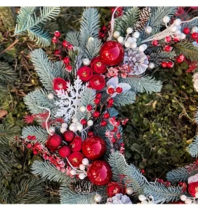 Detailed view of festive Christmas wreath featuring red roses, baubles, and frosty pine needles