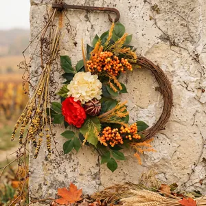 Ghirlanda del raccolto autunnale con zucca e ortensie appesa su un muro di pietra rustico.