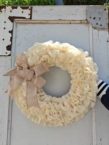 Crèmekleurige ruches stoffen krans met een grote rustieke jute strik aan een oude deur.