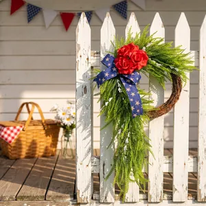 Couronne patriotique du 4 juillet avec roses rouges et ruban à étoiles sur une clôture blanche.