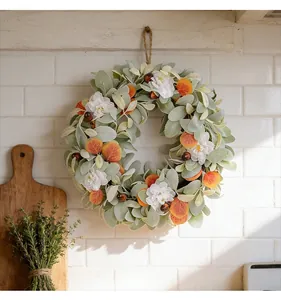 Vista detallada de corona otoñal con hojas de oreja de cordero y flores blancas en pared.