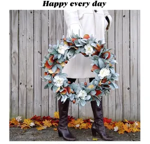 Artificial autumn wreath with white flowers and acorns held against wooden fence