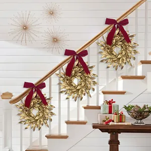 Christmas gold leaf wreaths with red velvet bows hanging on a white indoor staircase