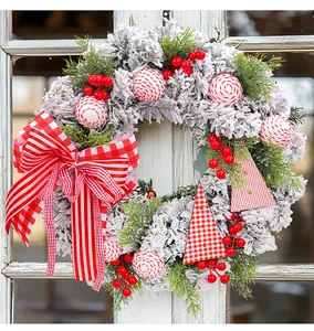 Detailaufnahme eines beflockten Weihnachtskranzes mit roten Beeren und Ornamenten