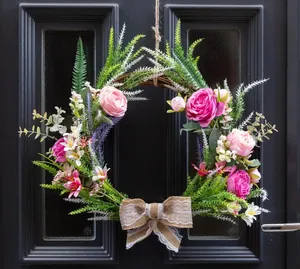 Detail view of a handcrafted artificial rose wreath with a rustic burlap bow on a dark door