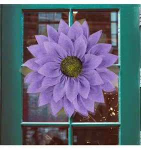 Close-up of a handmade purple burlap sunflower wreath hanging on a green door.