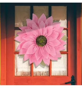 Detailed view of a pink burlap sunflower wreath hanging on a rustic red wooden door frame.