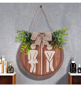 Detail of a farmhouse wooden restroom sign featuring burlap bow and green artificial leaves
