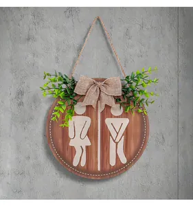 Close-up of a rustic wooden bathroom sign with funny toilet icons and greenery decoration