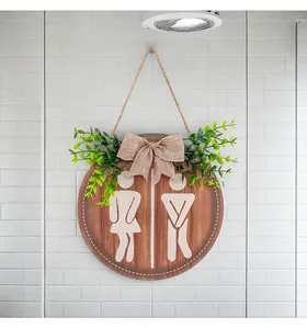Decorative round wooden restroom sign with burlap bow and faux greenery on white tiles