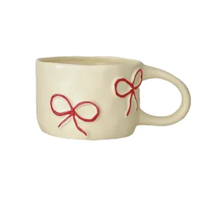 Tazza in ceramica crema con motivi a fiocco rosso disegnati a mano