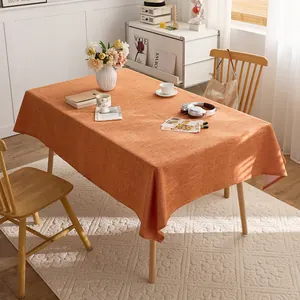 Detailed view of an orange linen-style tablecloth on a wooden table in a sunny room