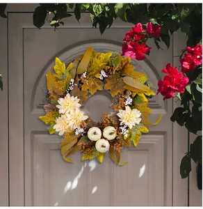 Detailansicht eines Herbstkranzes mit weißen Kürbissen und Ahornblättern an einer Tür.