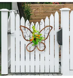 Corona de ramitas en forma de mariposa con flores amarillas colgada en una valla blanca