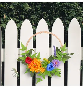 Détail d'une couronne de fleurs artificielles colorées avec perles en bois sur clôture.