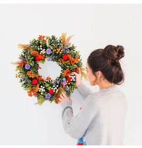 Detail of woman hanging a vibrant eucalyptus wreath with summer fruits on white wall
