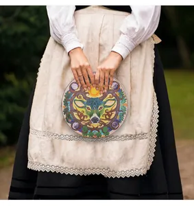 Handcrafted Shamanic drum with decorative deer and sun motifs held in traditional attire.