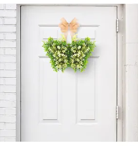 Corona de hojas verdes en forma de mariposa con lazo melocotón en una puerta blanca