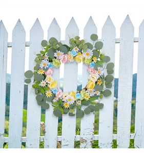 Gros plan d'une couronne florale de marguerites et roses sur une clôture en bois blanc