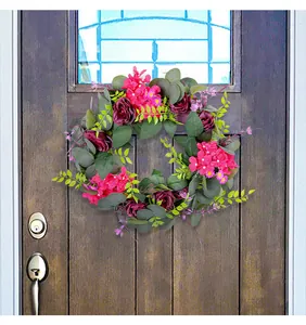 Detailbeeld van een krans met paarse rozen en roze bloemen op een rustieke houten deur.