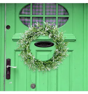 Artificial eucalyptus wreath with white flowers hanging on a green wooden door.