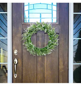 Lush green eucalyptus spring wreath with small white flowers displayed on a brown front door