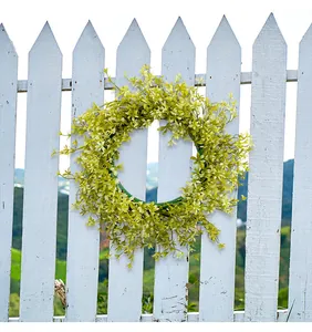 Kunstmatige geelgroene lentekrans die buiten aan een wit houten tuinhek hangt