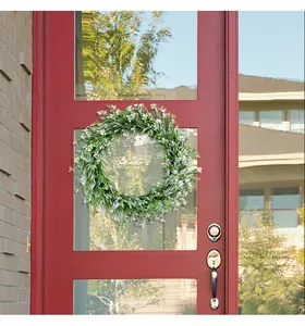 Decorative spring greenery wreath with small white flowers hanging on a classic red front door.
