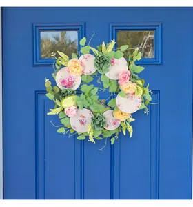 Corona decorativa primaverile con rose rosa e piatti di ceramica vintage su porta blu brillante