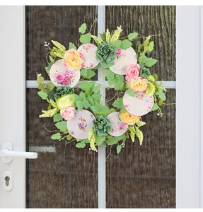 Ghirlanda primaverile decorativa con fiori rosa e piatti in ceramica sulla porta
