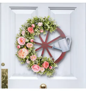 Decoratieve wagenwiel krans met roze pioenrozen en een lichtblauwe gieter op deur