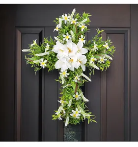 Corona di Pasqua a forma di croce con gigli bianchi e verde su una porta scura.